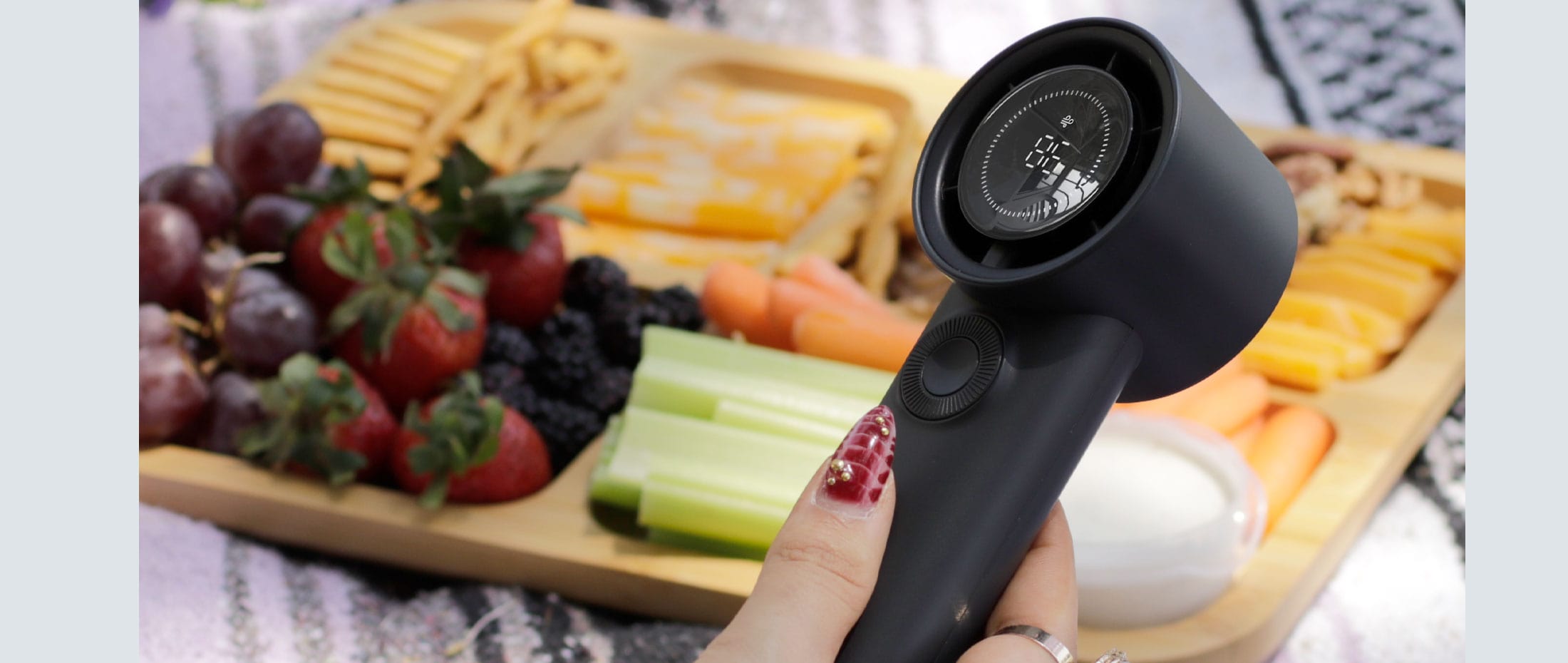 Handheld Aluratek fan with a wooden board of fruits and vegetables in the background