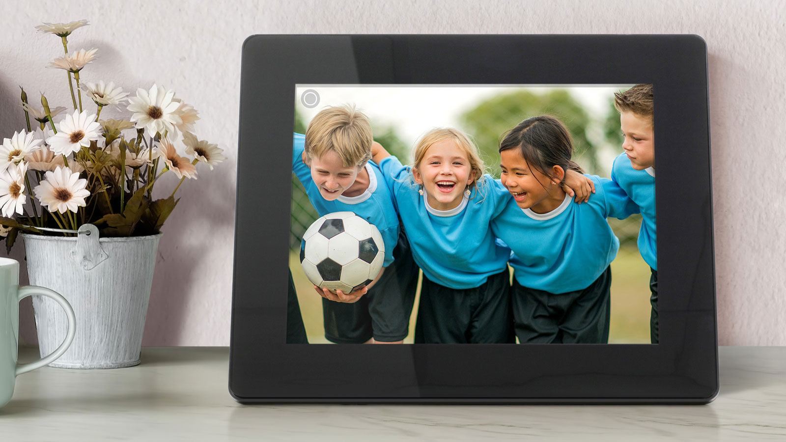 Aluratek digital photo frame sitting on a counter by a flower