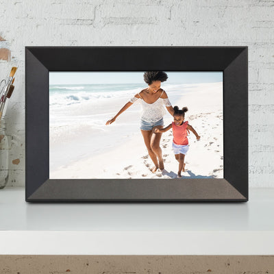Digital photo frame displaying a picture of a woman and child on a beach, against a white brick wall.